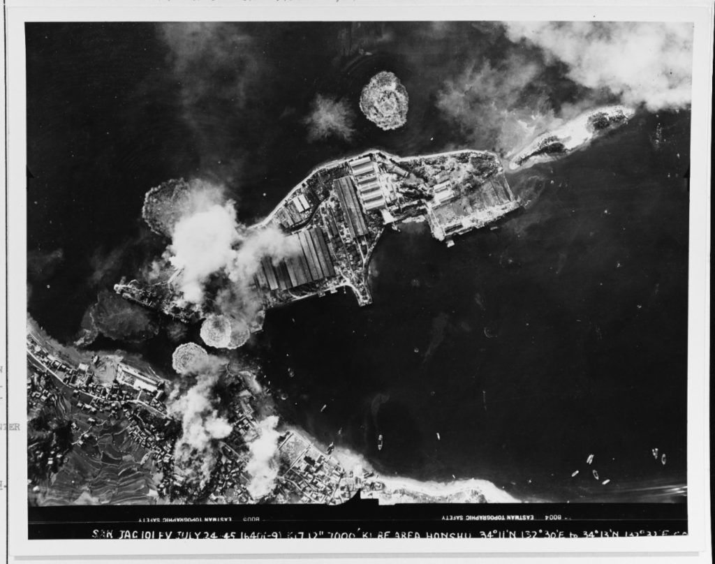 Japanese aircraft carriers under attack at Kure on 24 July 1945. Ship at left, receiving mostly bombs, is Amagi. Heavily camouflaged ship in right center is Katsuragi